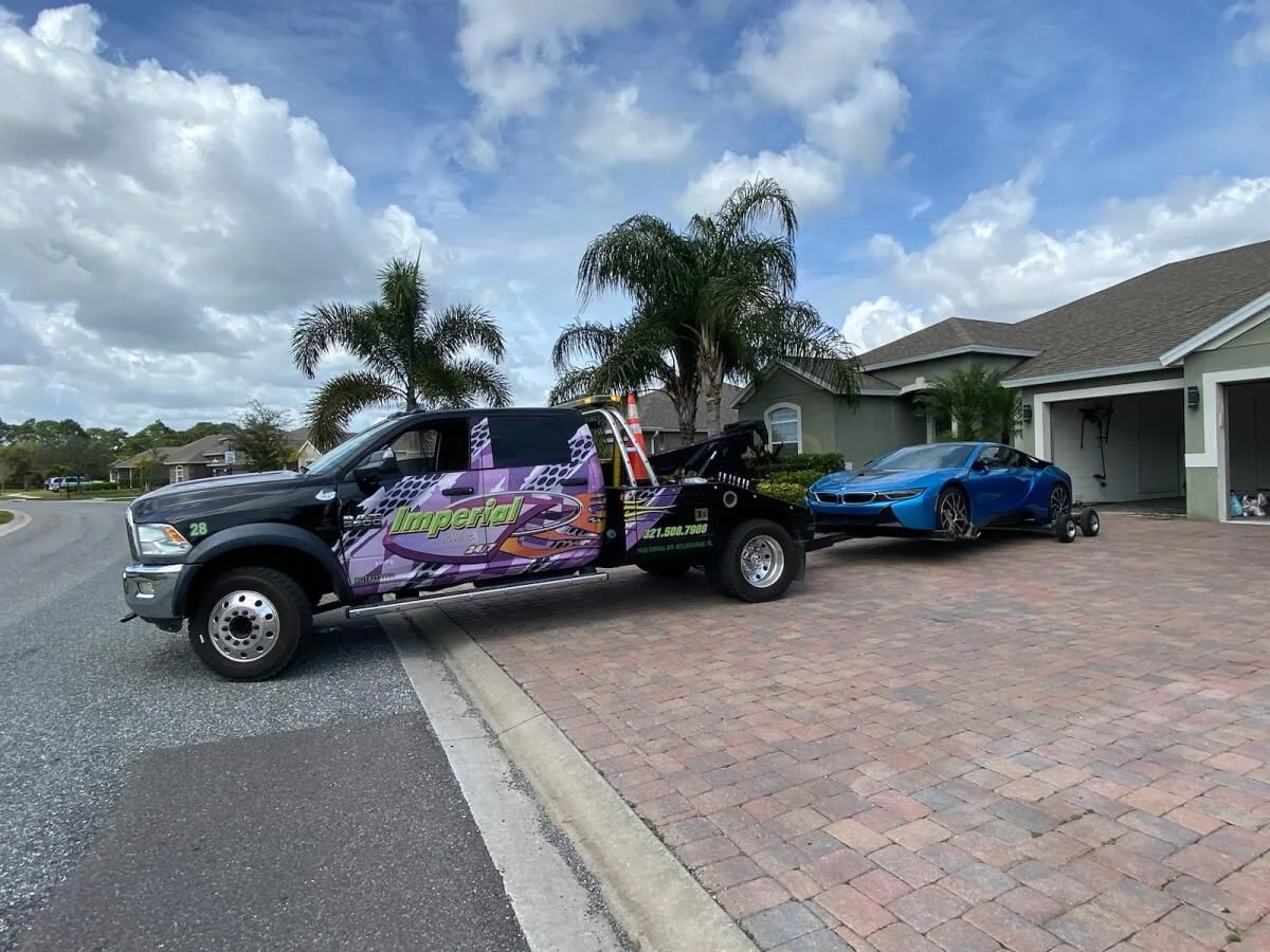Imperial Towing wrecker towing a blue BMW i8 from a Brevard County driveway