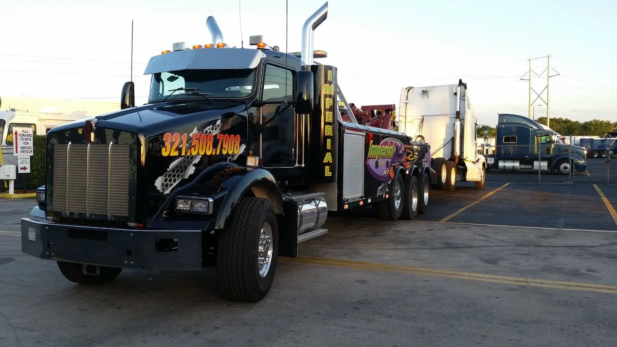 Imperial Towing black heavy wrecker recovering a semi truck at dusk in Florida