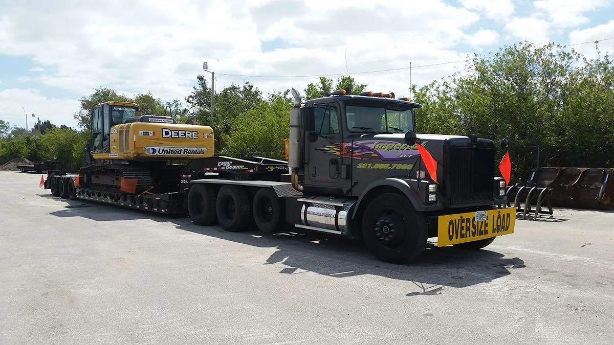 Imperial Towing heavy-haul truck transporting a John Deere excavator on a lowboy trailer in Melbourne, Florida